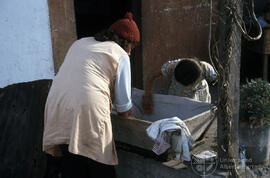 Mujer junto a niña pequeña lavando en una artesa