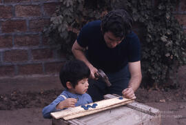 Hombre junto a niño pequeño clavando tapas metálicas en una tabla
